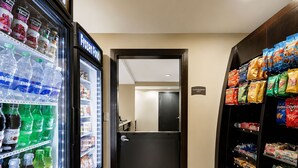 A hotel corridor with a frozen food refrigerator, snack shelves, and a door leading to a room. - ADA Suite Near NASA Goddard | Free Breakfast! (Lanham)