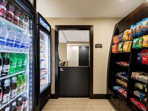 A hotel corridor with a frozen food refrigerator, snack shelves, and a door leading to a room. - ADA Suite Near NASA Goddard | Free Breakfast! (Lanham)