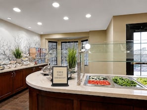 A buffet area with a sign indicating free daily breakfast, a variety of food options, and a modern interior design.