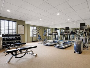 Een fitnessruimte met loopbanden, elliptische trainers, een bankdrukapparaat en gewichten.