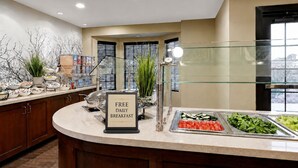 A buffet area with a sign indicating free daily breakfast, a variety of food options, and a modern interior design.