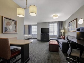 Ett hotellrum med en säng, ett skrivbord, en stol, en tv och en lampa.