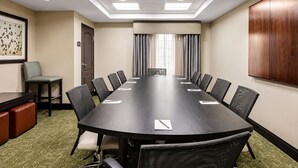 Une salle de conférence avec une longue table, des chaises, une porte, un tableau encadré et un meuble en bois.