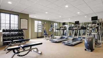 Une salle de remise en forme équipée de tapis de course, de vélos elliptiques, d’un banc de développé couché et d’haltères.