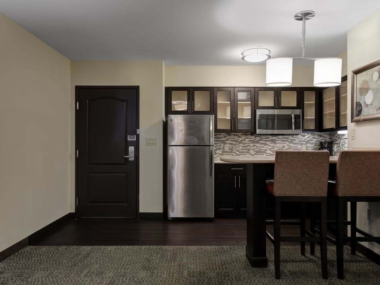 A compact kitchen with a refrigerator, microwave, and dark cabinets.