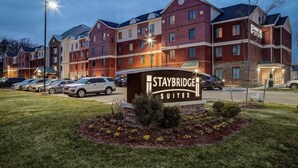 Un hotel Staybridge Suites con varios edificios, un estacionamiento y una entrada bien iluminada.