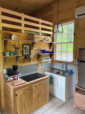 A wooden cabin kitchen with a built-in stove, a sink, and a window overlooking greenery.