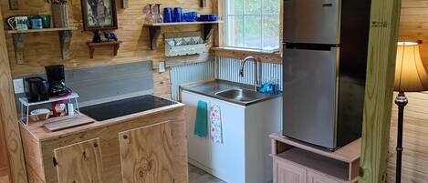 A compact kitchen with wooden cabinets, a stainless steel refrigerator, and a window providing natural light.