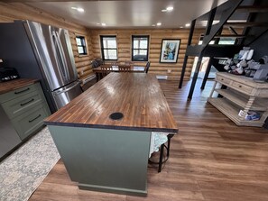 A kitchen with a central island, wooden walls, and a stainless steel refrigerator.
