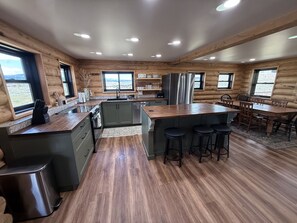 A modern log cabin interior with a kitchen, dining area, and bar stools. - Lazy J Madison Range Retreat (Cameron)