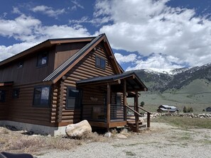 A log cabin with a porch and a mountain backdrop.