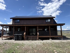 Une cabane en rondins à deux étages, dotée d’un porche, d’un espace extérieur couvert aménagé en salon et offrant une vue sur le paysage environnant.