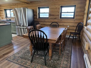 A wooden cabin interior with a dining table, chairs, a refrigerator, and a kitchen area. - Lazy J Madison Range Retreat (Cameron)