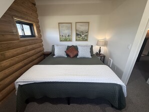 A room with a bed, a window, two paintings, a lamp, and a wooden wall.