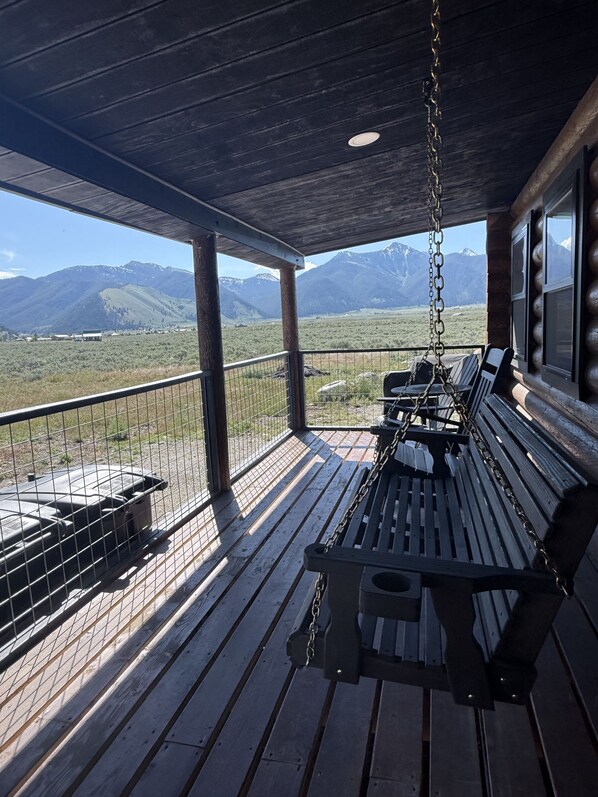 A wooden deck with a swing chair and a table, overlooking a mountainous landscape.