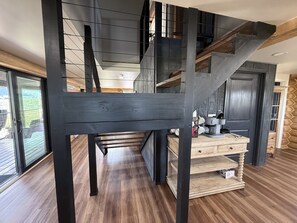 A modern interior with a wooden staircase, a kitchen area with a coffee machine, and a view through a glass door.