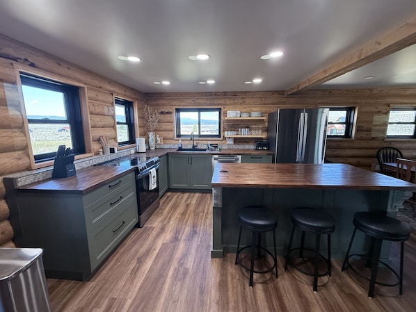 A modern kitchen with wooden walls, a large island with stools, and a view of the outdoors.