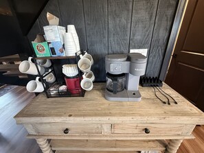 A coffee station with a Keurig coffee maker, a mug rack, and a coffee pod holder on a wooden table.