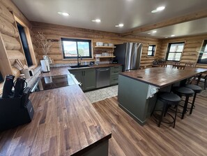 Une cuisine moderne dans un chalet en bois, dotée d’un îlot central, d’appareils électroménagers en acier inoxydable et offrant une vue sur l’extérieur.