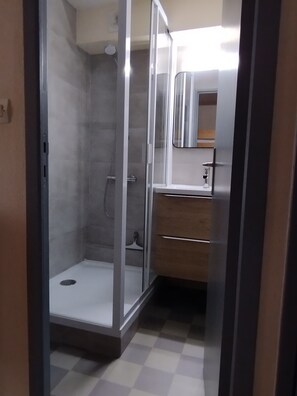 A bathroom with a glass shower enclosure, a sink with a mirror, and a wooden vanity.