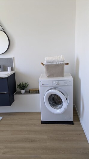 Une petite buanderie équipée d’un lave-linge à chargement frontal, d’une petite plante en pot et d’un meuble de couleur sombre.