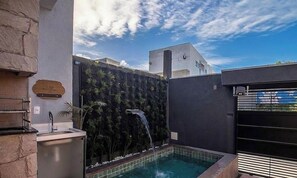 A modern outdoor pool area with a waterfall feature, stone walls, and a metal fence.