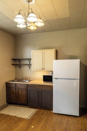 Une cuisine avec des meubles de rangement en bois, un réfrigérateur blanc, un four à micro-ondes et un luminaire suspendu.
