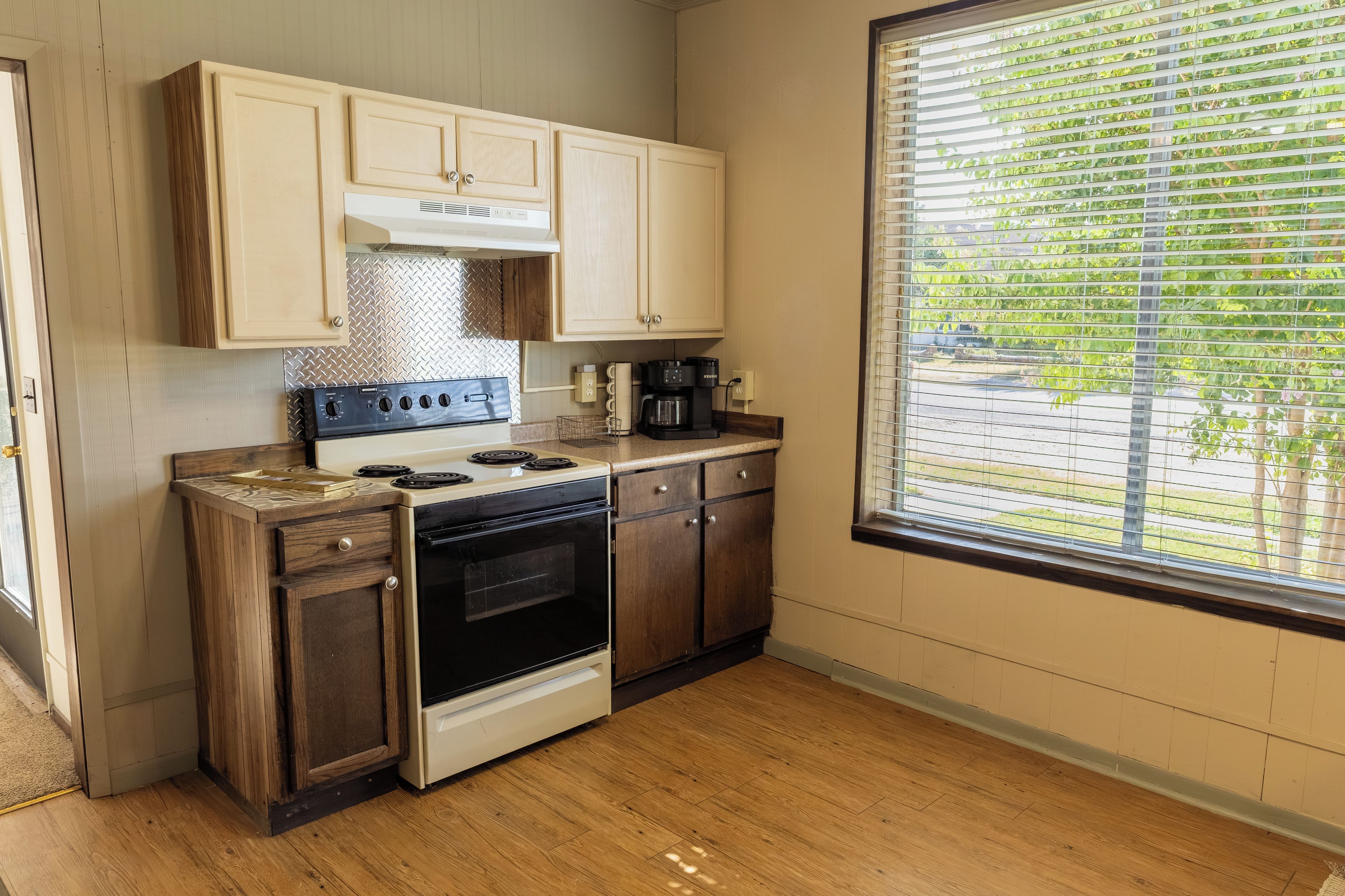 A kitchen with wooden cabinets, a stove, a coffee maker, and a window with blinds.