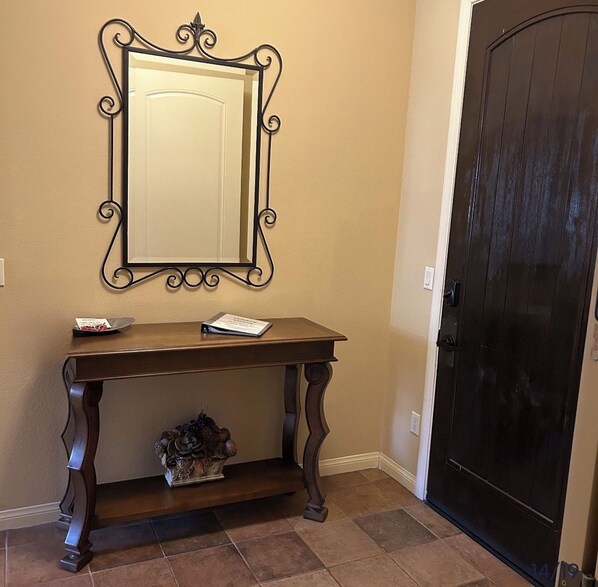 A dark wooden console table with a mirror above it, a small decorative item on the lower shelf, and a dark door to the right. - Beautiful Villa in La Quinta!
2-bedroom Legacy Villas AC, gym, gorgeous pools! (La Quinta)