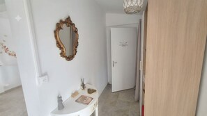 Ein Flur mit einer weißen Tür, einem Spiegel und einem kleinen Tisch mit einem Notizbuch und Dekoration.