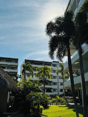 A modern hotel with multiple floors, a well-maintained lawn, and palm trees. - Beautiful 2 Bedroom with A/C, BBQ, and Pools (Nuevo Nayarit)