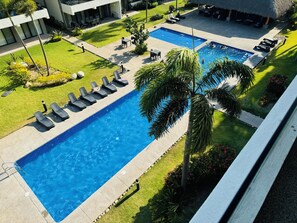 Ein Pool mit Liegestühlen, einer Palme und einem Gebäude im Hintergrund.