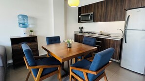 A modern kitchen with a wooden dining table, blue upholstered chairs, a built-in microwave, and a stainless steel refrigerator. - Beautiful 2 Bedroom with A/C, BBQ, and Pools (Nuevo Nayarit)