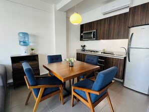 A modern kitchen with a wooden dining table, blue upholstered chairs, a built-in microwave, and a stainless steel refrigerator. - Beautiful 2 Bedroom with A/C, BBQ, and Pools (Nuevo Nayarit)