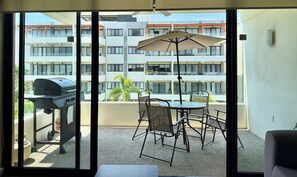 A balcony with a grill, outdoor seating, and a view of a multi-story building. - Beautiful 2 Bedroom with A/C, BBQ, and Pools (Nuevo Nayarit)