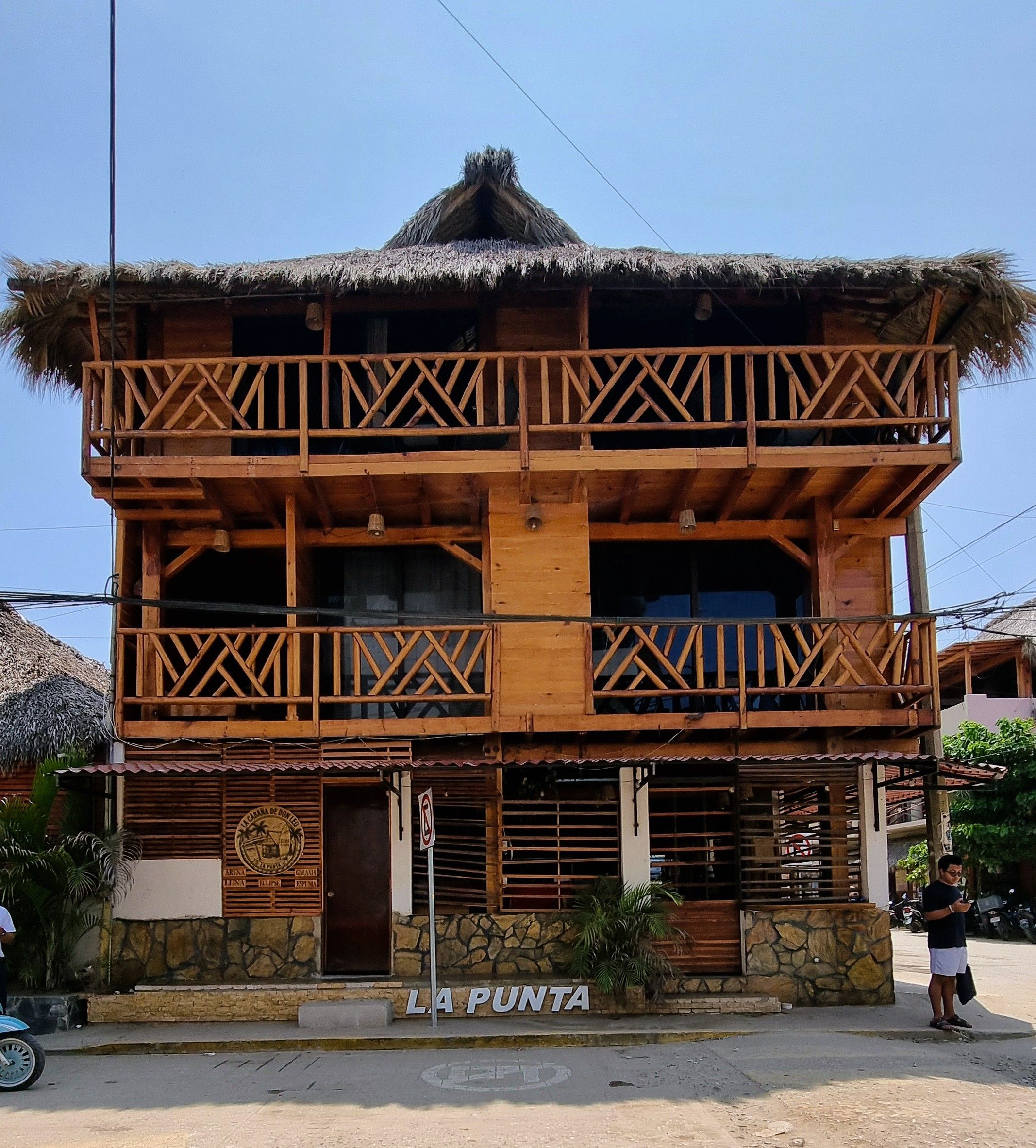 Un edificio de madera de dos pisos con techo de paja, un balcón con barandillas de madera y un letrero que dice 'LA PUNTA'.