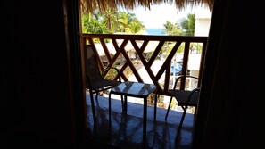 Un balcó amb dues cadires i una taula, amb vista a un paisatge tropical de palmeres i al mar.