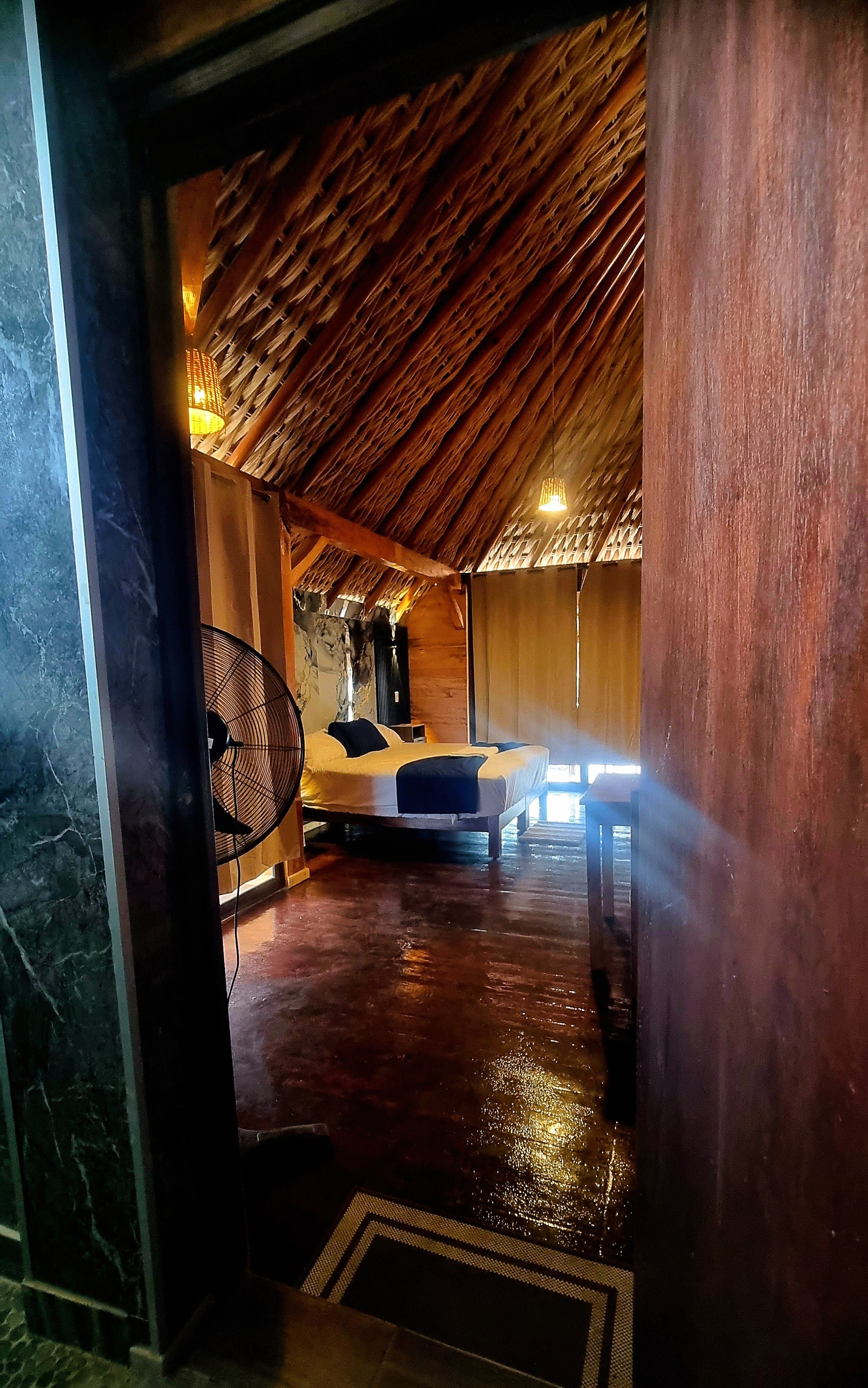 Una habitación con techo inclinado, una cama, un ventilador y una pared con textura.