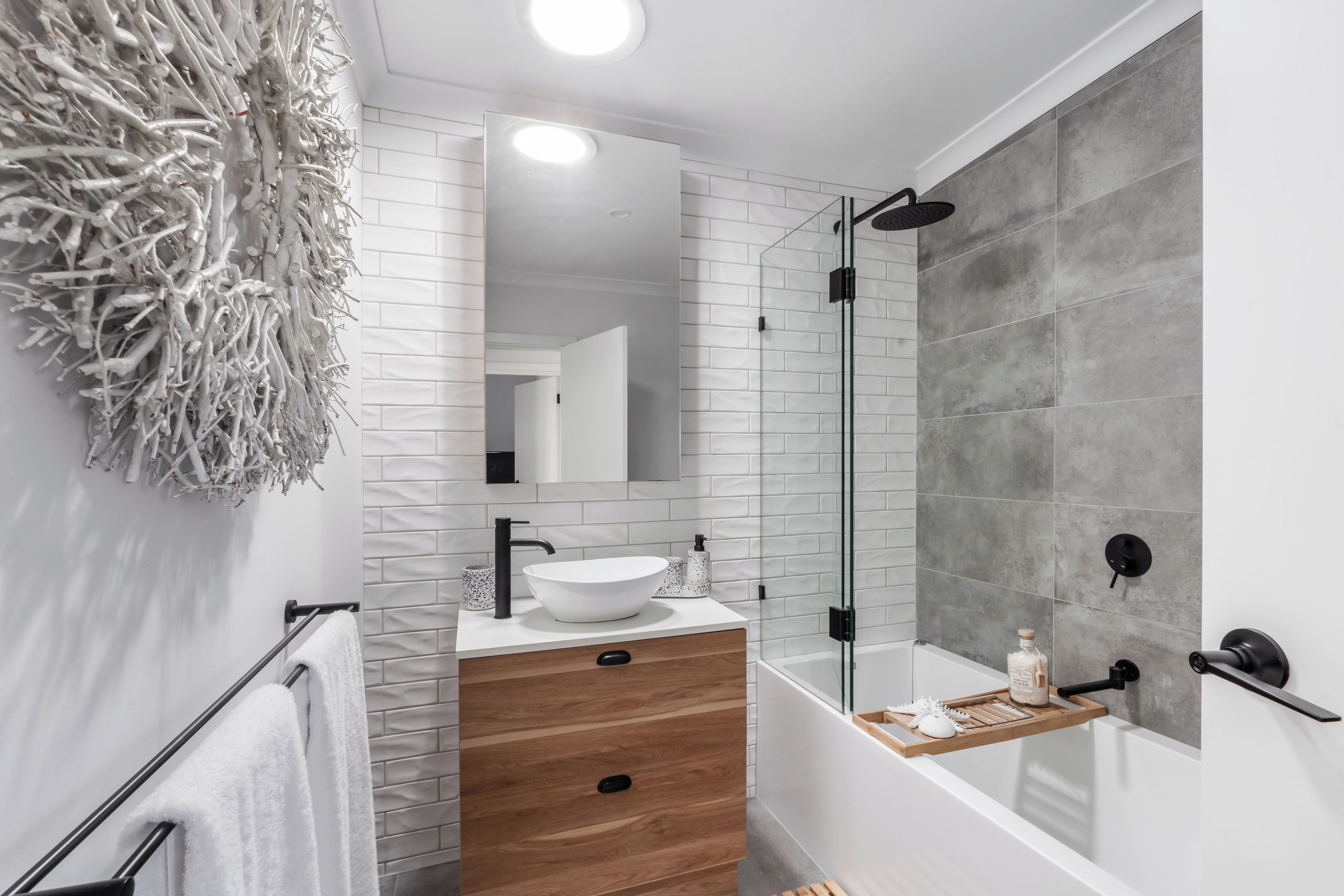 A modern bathroom with a white sink, wooden vanity, and a glass shower enclosure.