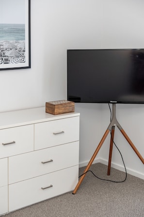 A modern room with a white dresser, a flat-screen TV on a tripod stand, and a framed picture on the wall. - Sundrift A Contemporary Poolside Sanctuary (Rosebud)
