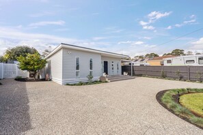 A single-story house with a gravel driveway, a small front yard with a tree, and a covered outdoor area. - Sundrift A Contemporary Poolside Sanctuary (Rosebud)