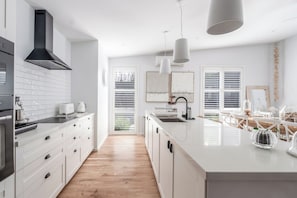 A modern kitchen with white cabinetry, a black range hood, and pendant lighting. - Sundrift A Contemporary Poolside Sanctuary (Rosebud)