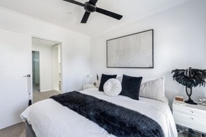 A bedroom with a bed, a ceiling fan, a bedside table, a lamp, and a wall-mounted artwork. - Sundrift A Contemporary Poolside Sanctuary (Rosebud)