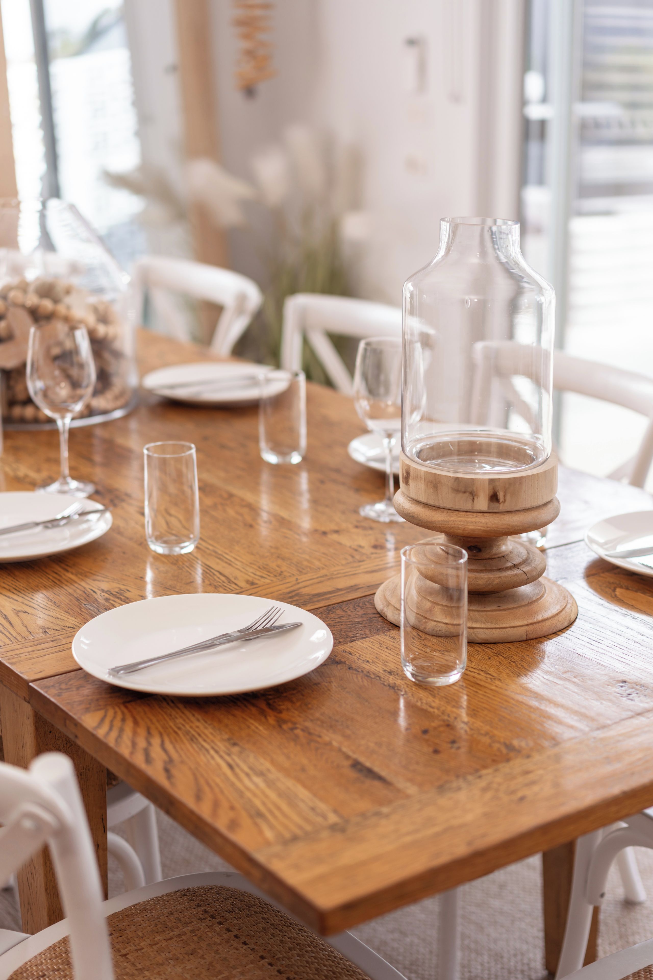 A wooden dining table set with plates, cutlery, and clear glassware.