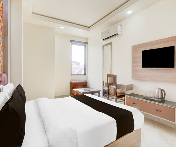 A hotel room with a bed, a desk with a chair, a television mounted on the wall, and a window.