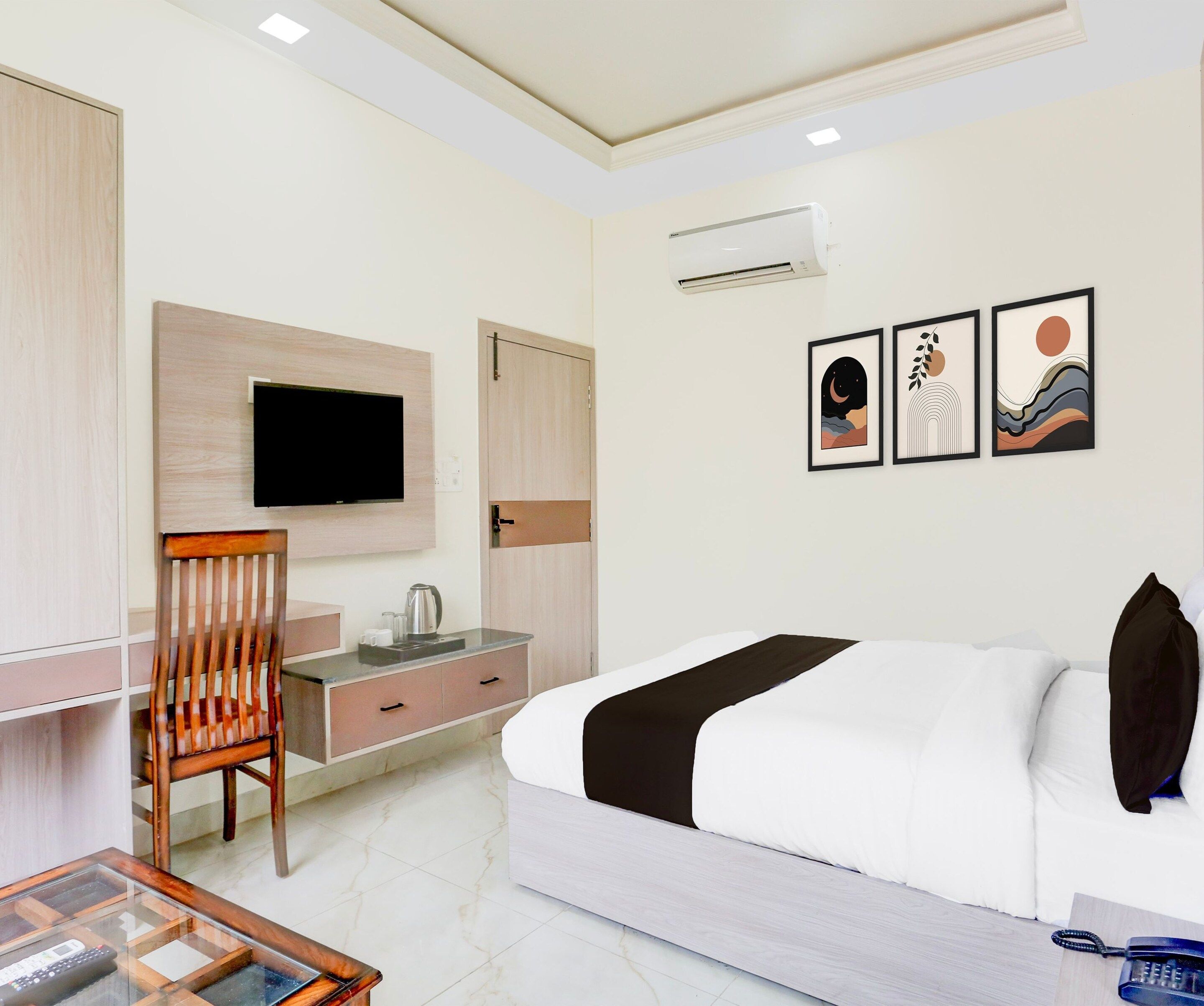 A hotel room with a bed, a desk with a chair, a flat-screen TV, a coffee maker, and three framed pictures on the wall.