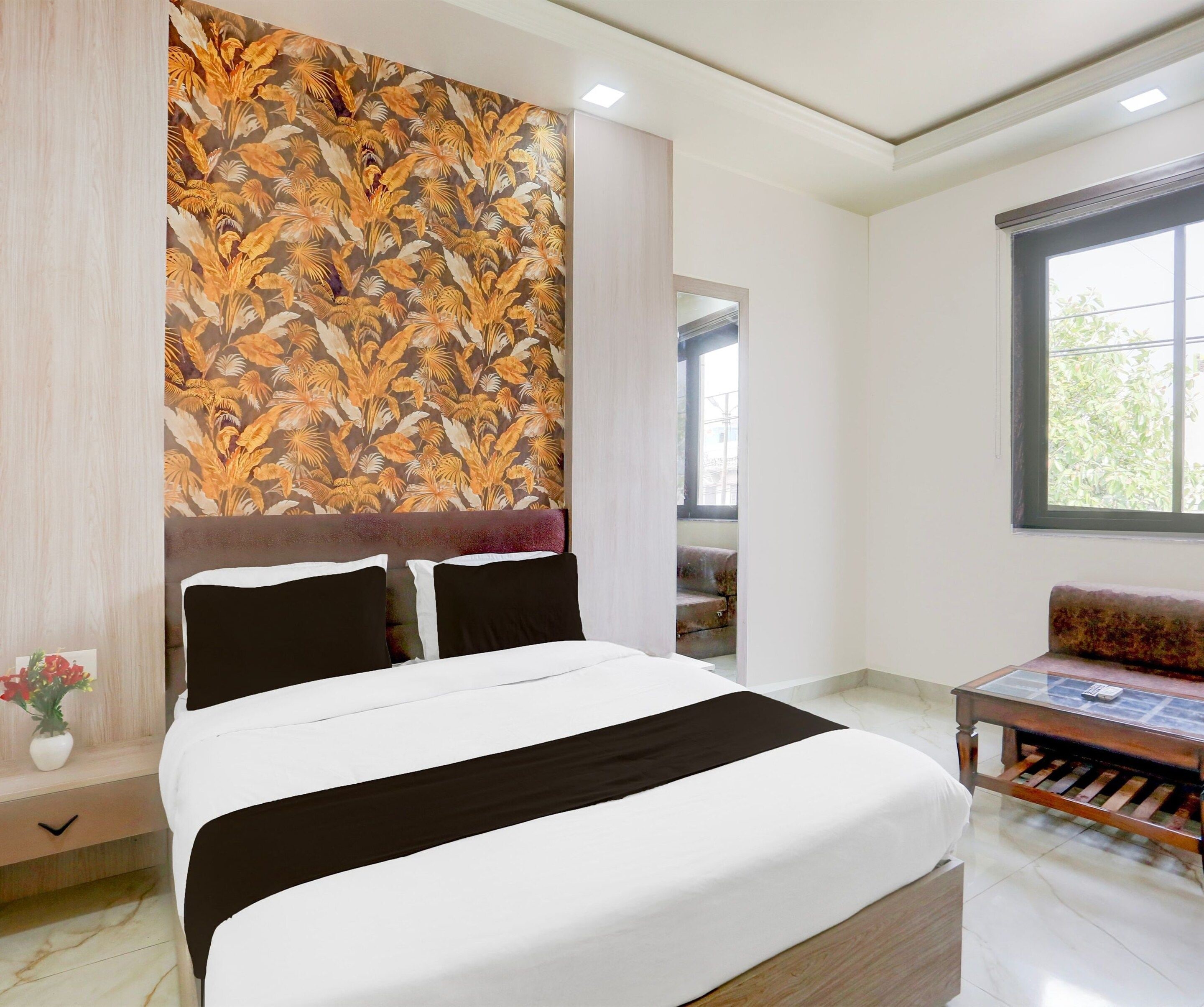 A hotel room with a bed, a sofa, a wall with a tropical leaf pattern, and a window.