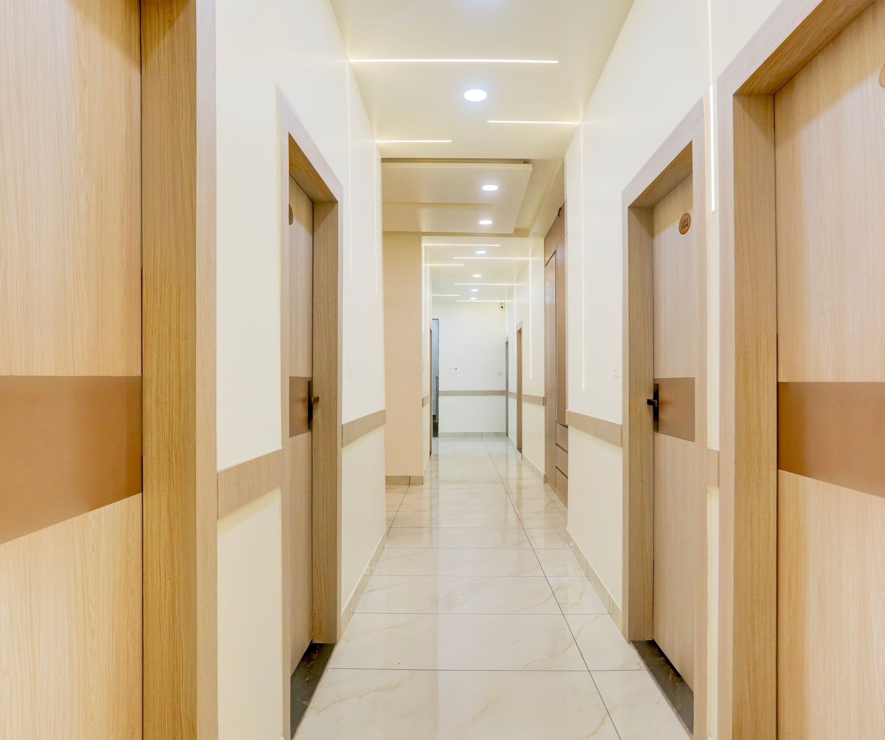A hotel corridor with wooden doors, recessed lighting, and a tiled floor.