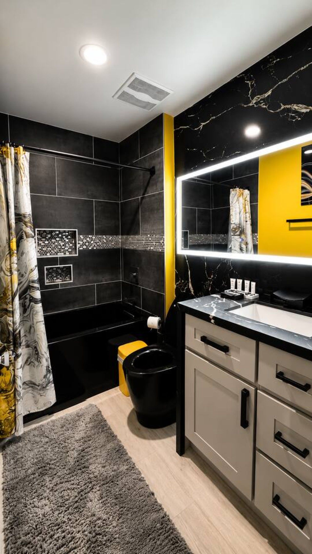 A modern bathroom with a black and yellow color scheme, a large mirror, and a toilet.