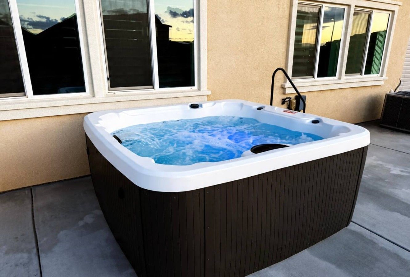 A hot tub with a wooden exterior, positioned on a concrete patio next to a building with large windows.